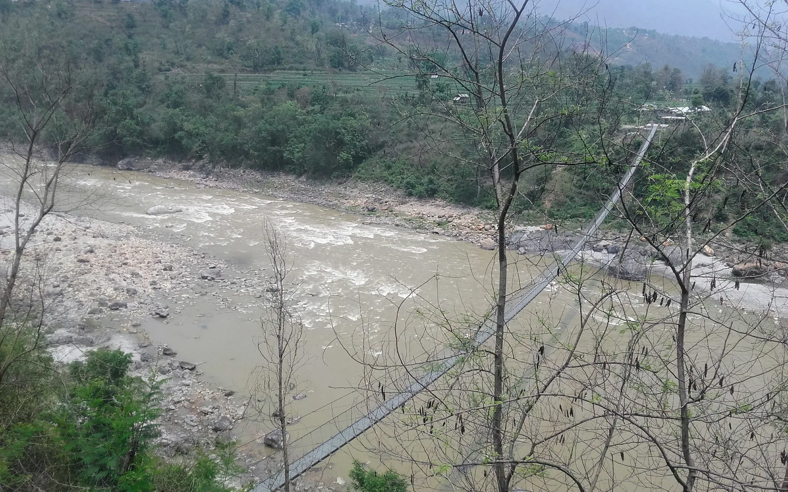 A steel suspension footbridge crossing a Himalayan river through green Nepali hills — photo by goFLY founder Mahabub Alam Razu, May 2017